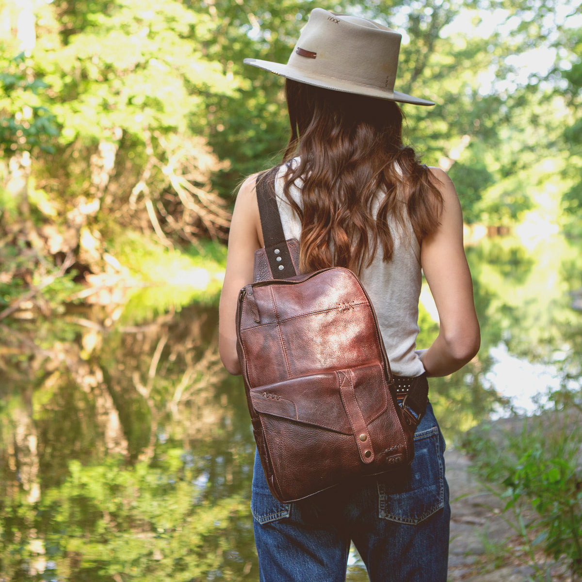 A durable woman wearing a Boss hat standing by a river. (brand name: Bed Stu)