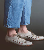 Person wearing playful Decoy lace-up derby shoes by Bed Stu, handcrafted in Italy, paired with blue denim pants against a dark background.