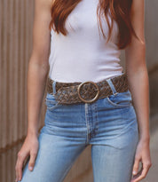 A person wearing the "Dreamweaver" white sleeveless top and high-waisted jeans from Bed Stu, along with a woven belt featuring a brass-tone buckle, stands against a neutral background, exuding a touch of vintage allure.