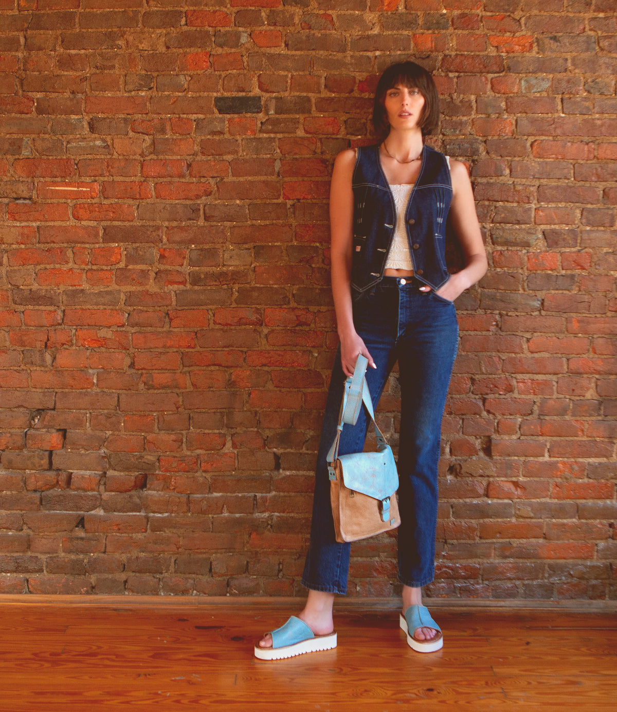 A stylish woman standing against a brick wall, exuding comfort in her Bed Stu Fairlee II leather slide sandals.