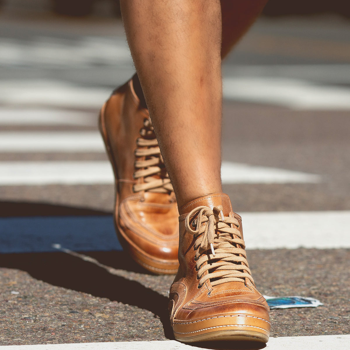 Close-up of a person walking on a city street wearing the Bed Stu Formation high-top sneakers in tan leather with a modern design.