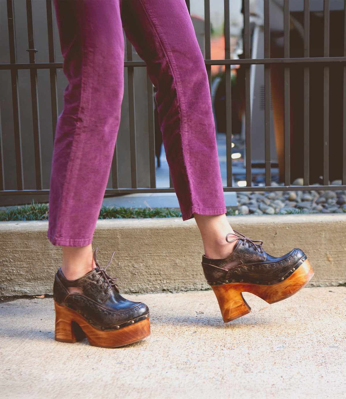 A person wearing Bed Stu's Karaoke purple pants and chunky wooden platform shoes, reminiscent of the 70s era, strides confidently down a concrete path.