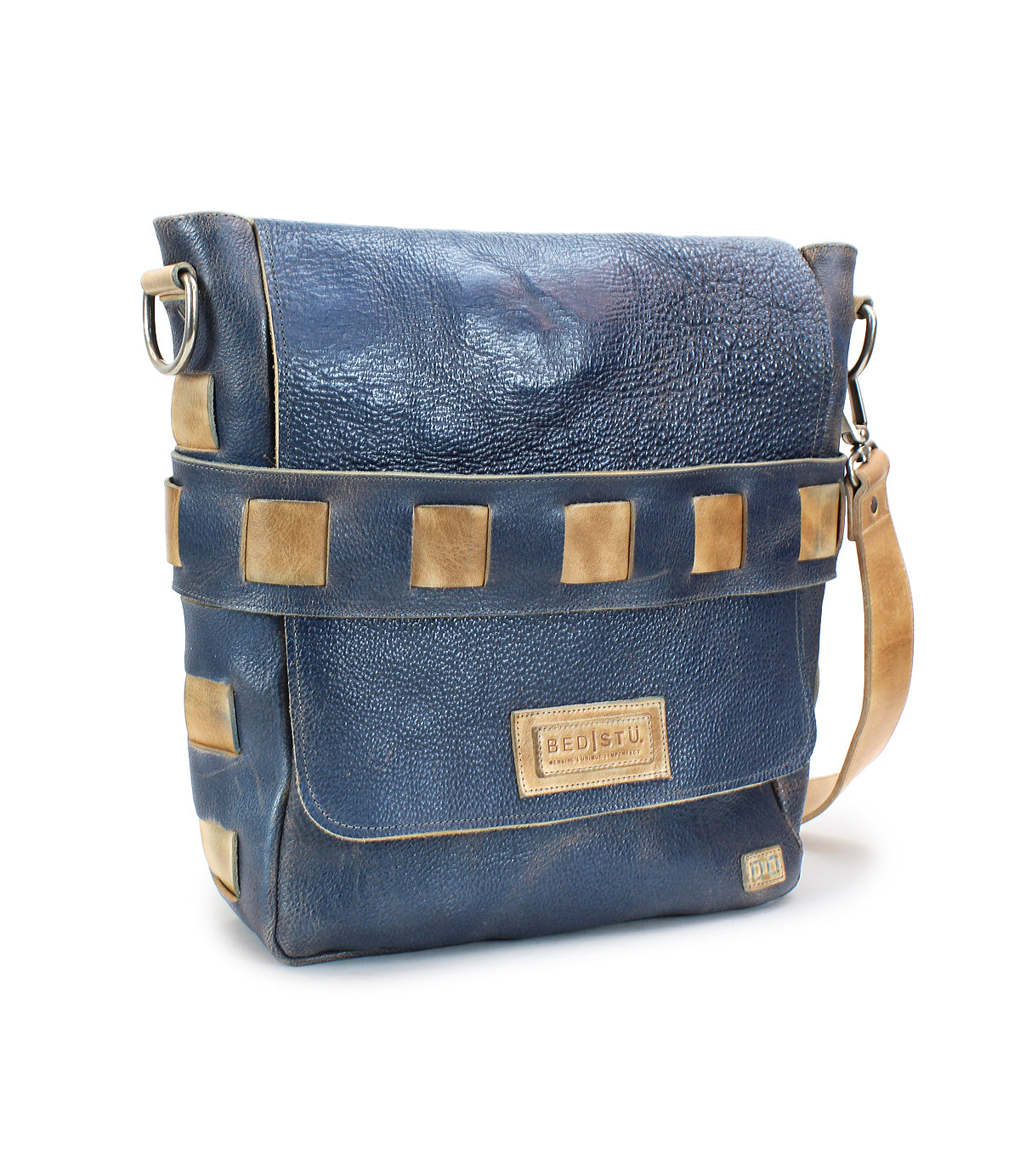 A handmade leather messenger bag in blue with tan accents, featuring a front flap closure and an adjustable beige shoulder strap. Crafted from vegetable-tanned leather, the Kure boasts an organic cotton-lined interior and a "Bed Stu" label on the front.