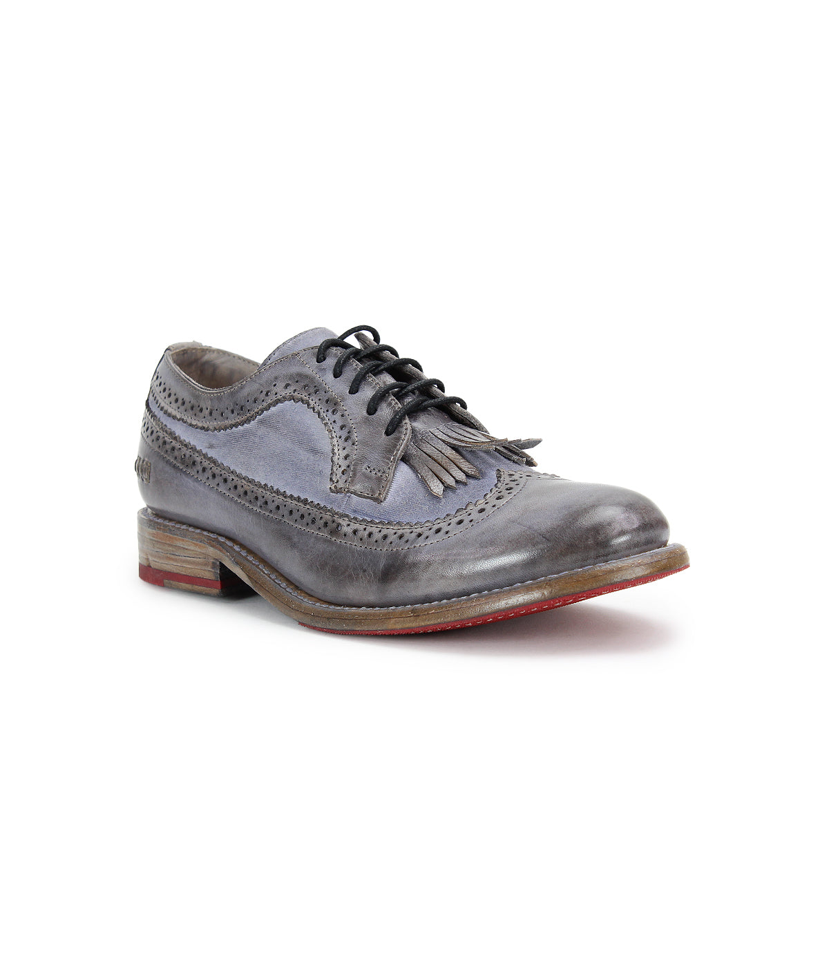 A single gray brogue shoe with detailed stitching, black laces, a low wooden heel featuring partial serrations and perforations, and a removable kiltie for added versatility. The product is the Lita K by Bed Stu.