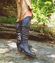 A woman in Bed Stu Leilani black boots standing on a rock in the woods.