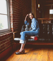 A woman sitting on a black couch in her office, wearing Bed Stu high-heeled shoes.