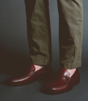 A person wearing olive green pants and Bed Stu Moat loafers stands against a dark background, exuding timeless sophistication.