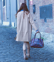 A person walking down a cobblestone street in a tan coat and brown boots carries the Bed Stu Rockababy, the ideal combination of style and function on their stroll.