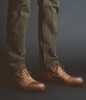 Person wearing olive green pants and Scoot leather dress shoes by Bed Stu, handcrafted in Italy, stands against a dark background.