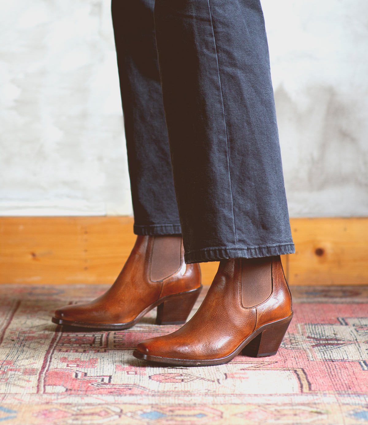 A woman exuding sartorial elegance wearing a pair of Bed Stu Viscera Chelsea boots on a plush rug.