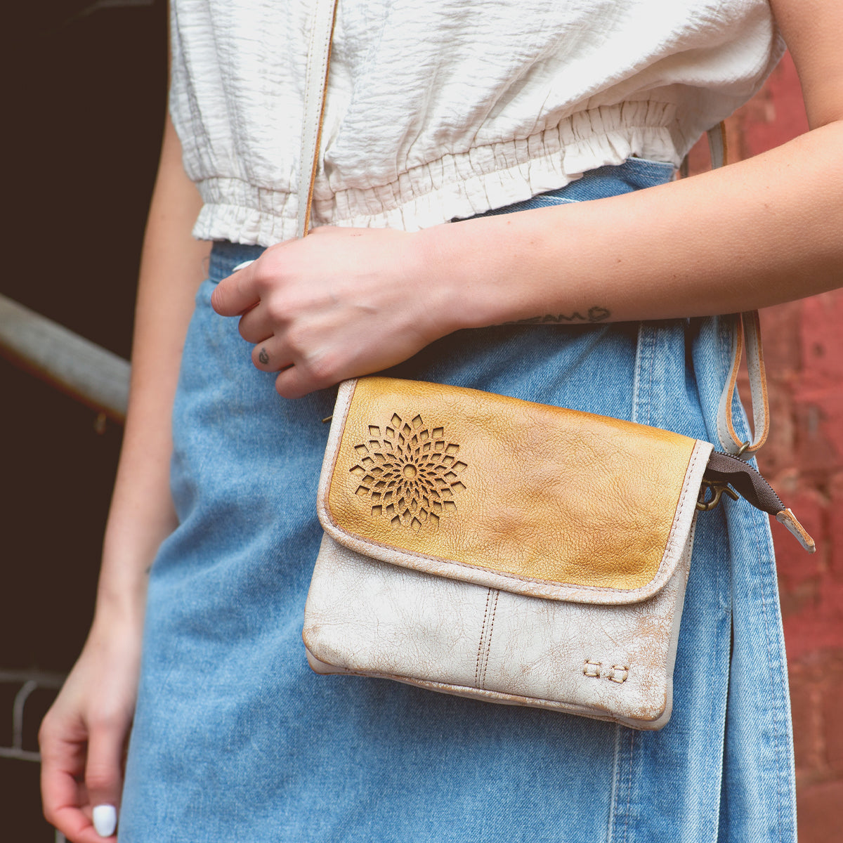 A woman wearing a denim skirt and carrying a stylish Bed Stu Ziggy II crossbody bag with compartments.