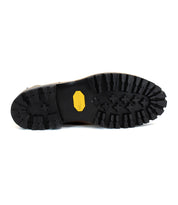The image shows the underside of a Brady Trek boot with a black rubber sole, featuring a rugged tread pattern and a yellow Bed Stu logo at the center.