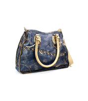 The Bruna by Bed Stu is a vintage-style blue leather handbag with beige handles, showcasing artisanal craftsmanship with a stitched X pattern design on the front.