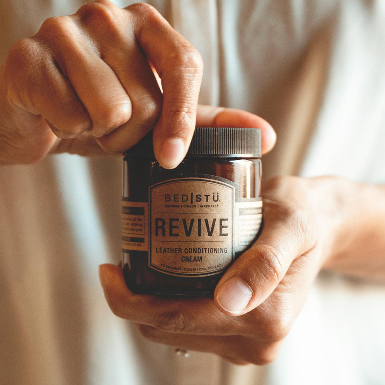 A person holding a jar of Revive Leather Cream (Bed Stu).