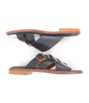 A pair of black slip on Italian leather sandals with a gold buckle product shot.