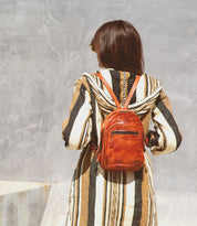 A woman wearing a striped dress and a brown leather Bed Stu Dominique backpack.