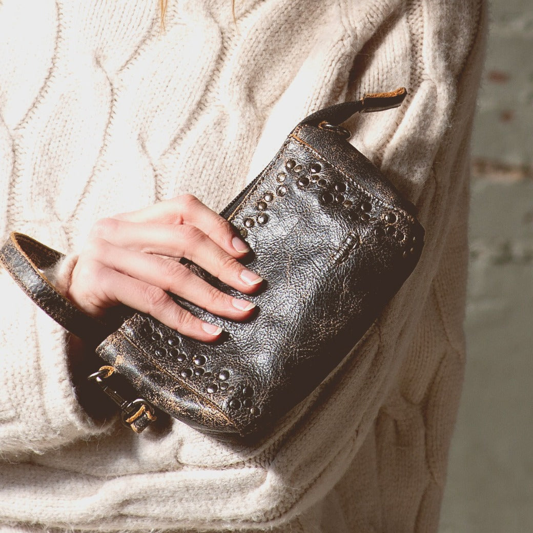 A woman wearing a sweater holding a Bed Stu Encase leather purse.