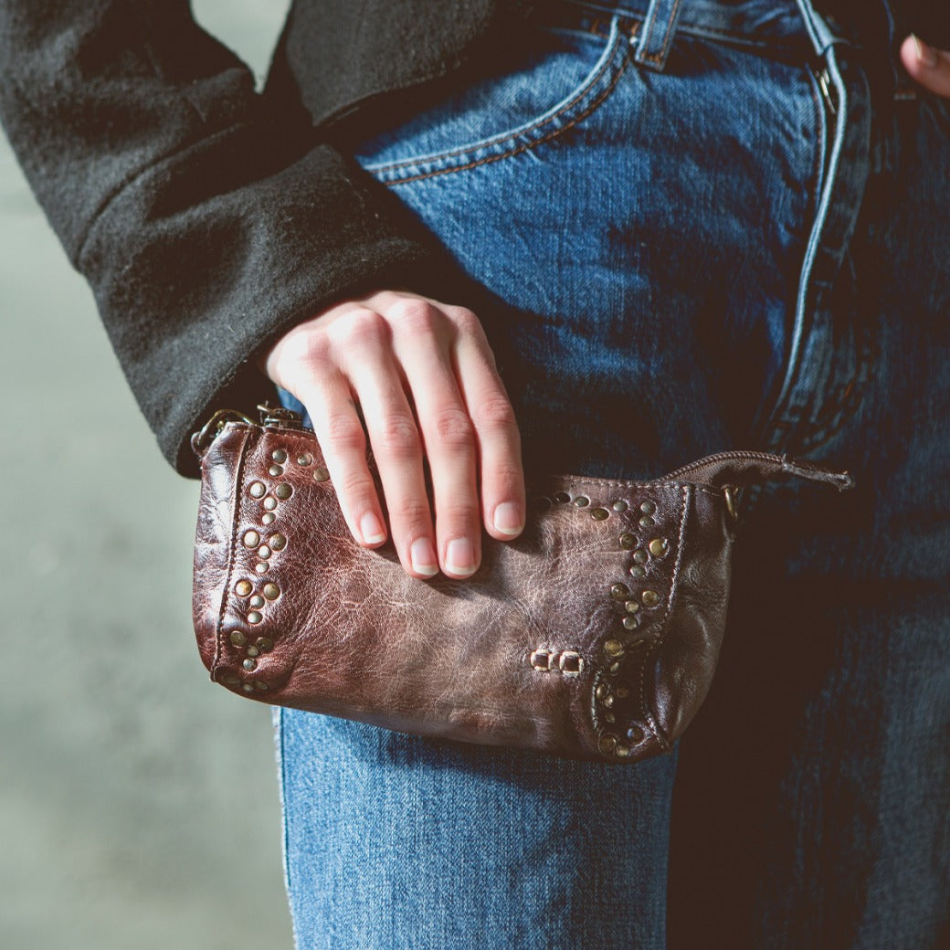 A woman holding a Bed Stu Encase brown leather purse.