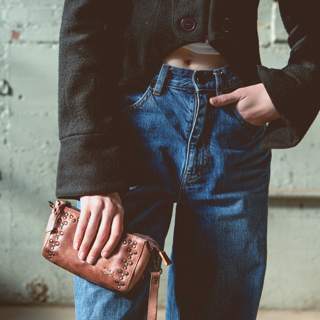 A woman wearing jeans and a jacket holding an Encase purse by Bed Stu.