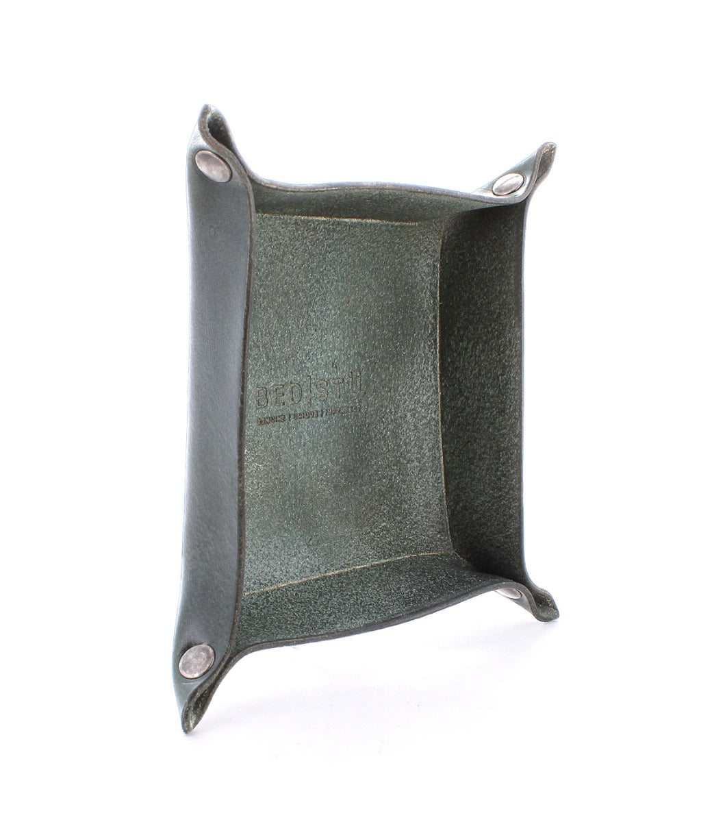 A square, green leather catchall tray with metal snap buttons at the corners for storing loose change and keys. The Expanse Catchall Tray by Bed Stu is embossed inside.