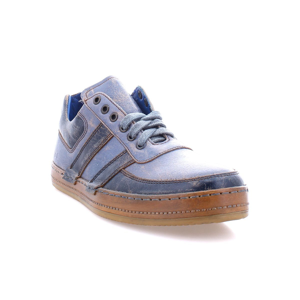 A side-angle photograph on a white background showcases a single Firepower men's sneaker in blue leather with brown accents and leather stripe details, featuring laces and a vulcanized rubber sole. The stylish design represents the craftsmanship of Bed Stu.