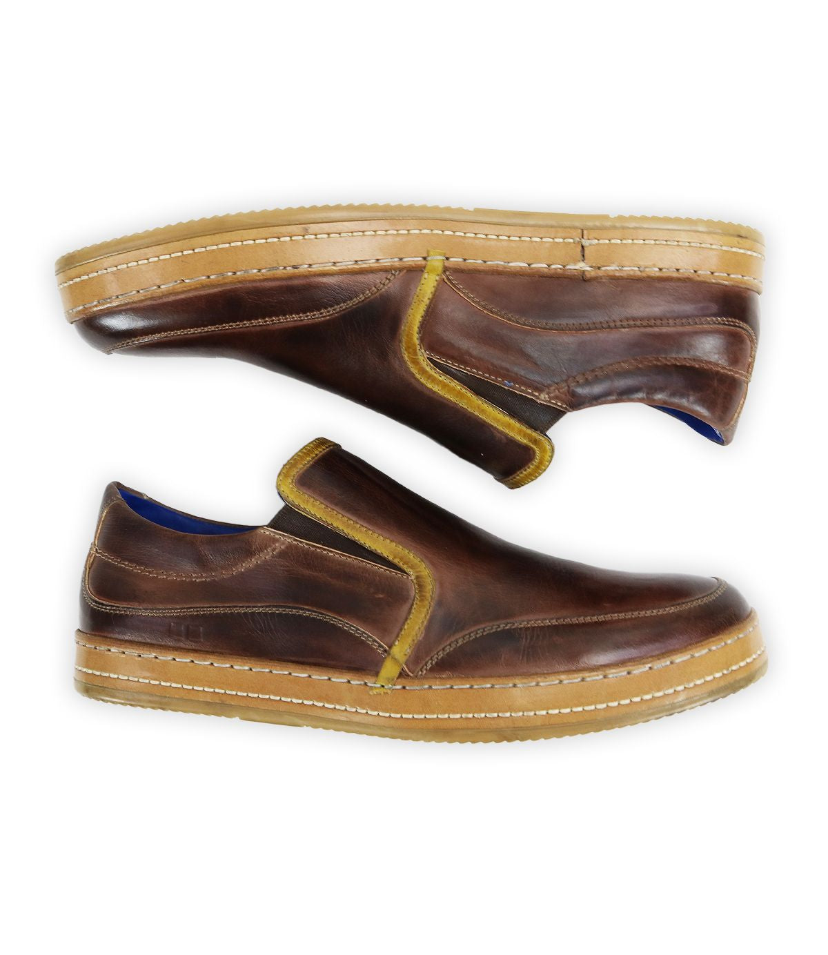 The Bed Stu Freestyle shoes are a pair of brown leather slip-ons with yellow accents and tan rubber soles, shown from the side to highlight their casual sophistication.