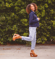 A woman in Bed Stu jeans and a Bed Stu denim jacket posing in front of bushes.