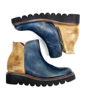 The Lydyi ankle boots by Bed Stu come in blue and tan leather, featuring side zippers and wavy black soles, viewed from the side. They are equipped with a lightweight platform outsole for added comfort.