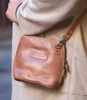 A woman is holding a Bed Stu Ventura tan leather crossbody bag.