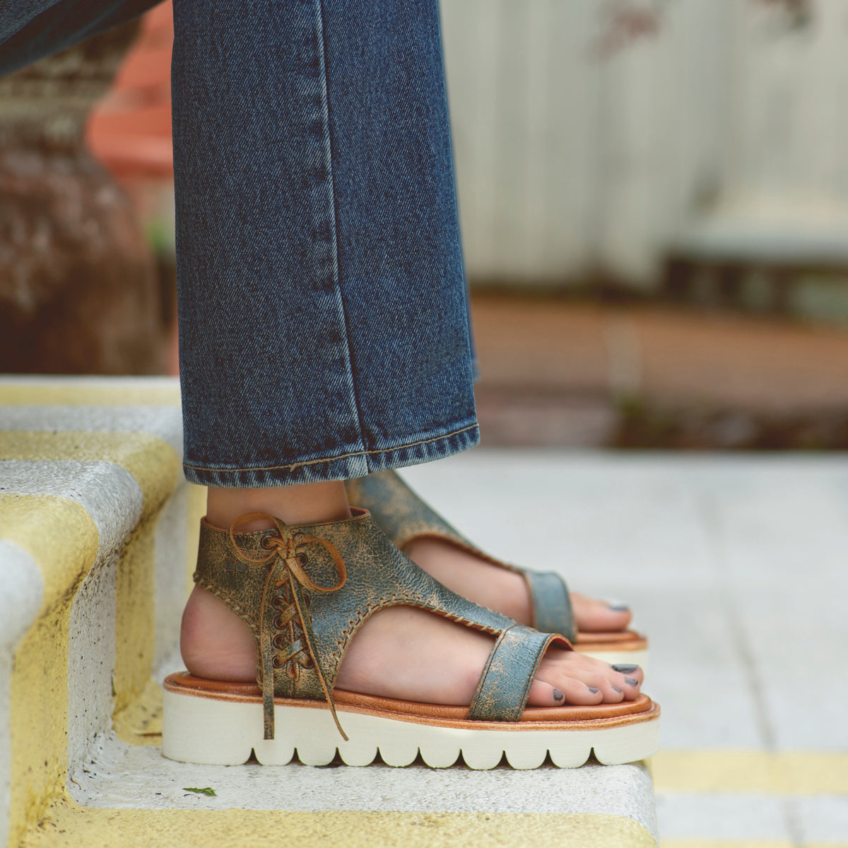 A woman wearing Bed Stu jeans and Bed Stu sandals standing on steps.